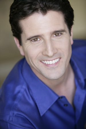 A man with white teeth and blue shirt smiling.